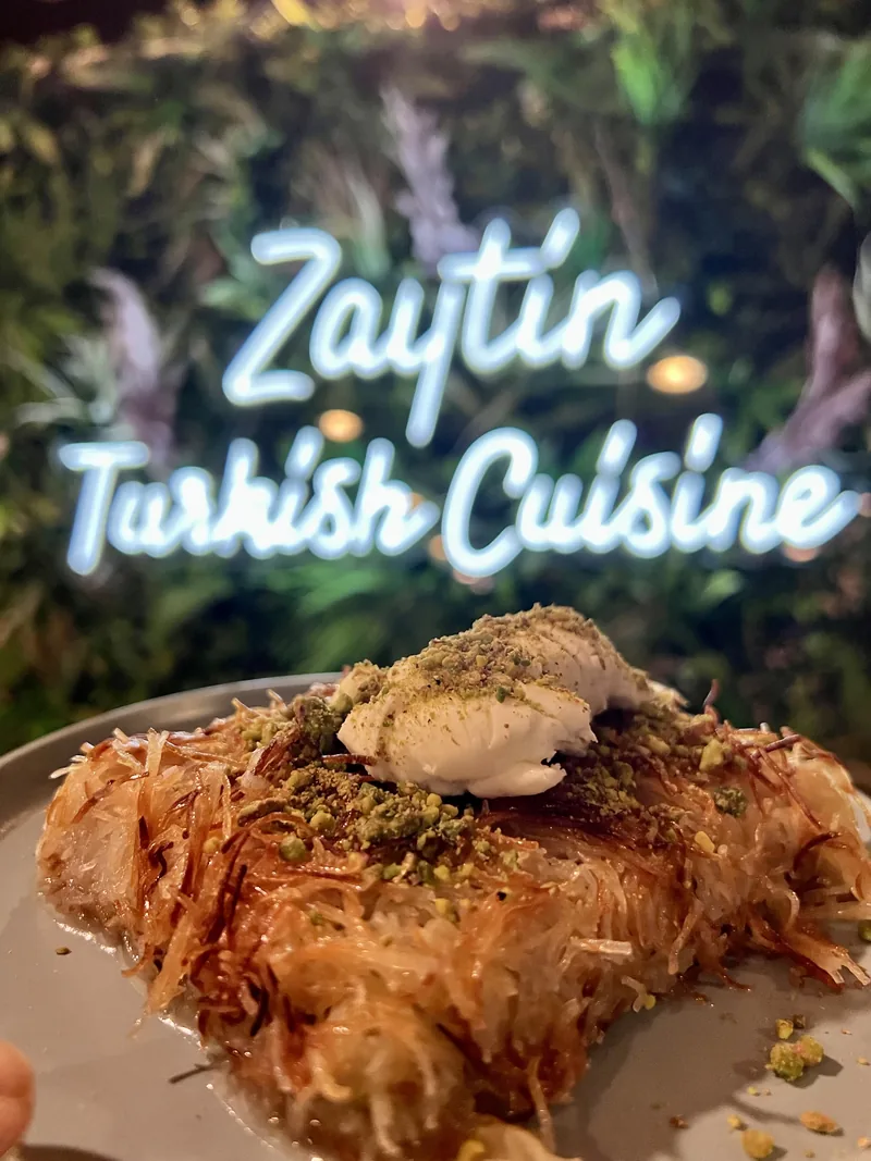 Künefe with clotted cream in front of the neon Zaytin sign